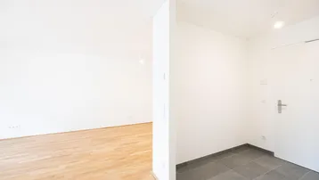 Heller Eingangsbereich mit Fliesenboden, der zu einem Zimmer mit Parkettboden führt.
