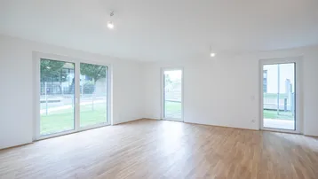 Heller Wohnraum mit mehreren Fenstern, hellem Parkettboden und Zugang zum Garten.