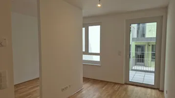 Helles Zimmer mit Parkettboden und Zugang zu einem Balkon, Blick auf den Innenhof.