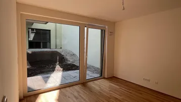 Helles Zimmer mit Holzboden und Zugang zu einem kleinen Außenbereich, ideal als Wohn- oder Schlafzimmer.