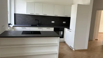 Moderne Einbauküche mit weißen Schränken, dunkler Arbeitsplatte und Kochinsel auf Fischgrätparkett.