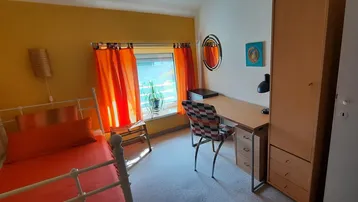 Helles Schlafzimmer mit gelben Wänden, Teppichboden, Bett, Schreibtisch und Kleiderschrank.