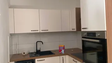 Moderne Einbauküche mit weißen Schränken, Holz-Arbeitsplatte und integriertem Geschirrspüler und Backofen.