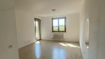 Helles Zimmer mit Laminatboden, Fenster und Zugang zu einem Außenbereich, der viel natürliches Licht hereinlässt.