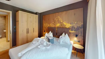 Gemütliches Schlafzimmer im alpinen Stil mit Holzkleiderschrank und Wandbild einer Berglandschaft.