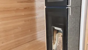 Moderner Holzofen mit Sichtfenster und Holzscheiten in einem Raum mit Holzwänden.