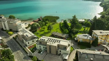 Luftaufnahme eines modernen Wohnkomplexes am Seeufer mit Bergblick und umliegender Natur.