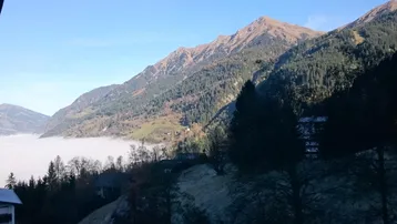 Majestätische Berglandschaft mit nebelverhangenem Tal und bewaldeten Hängen unter klarem Himmel.