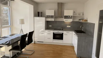 Moderne Küche mit Essbereich, hellen Fronten, grauer Arbeitsplatte und Holzboden.