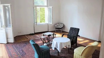 Helles Wohnzimmer mit Parkettboden, Teppich und Blick ins Grüne durch das offene Fenster.