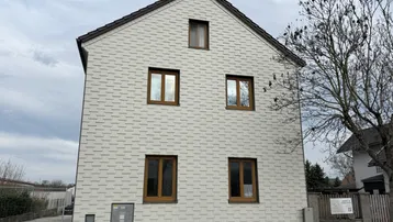 Giebelseite eines Hauses mit Schindelfassade, Satteldach und braunen Holzfenstern.