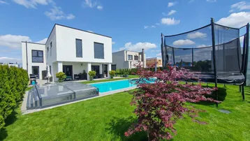 Geräumiger Gartenbereich mit modernem Pool, großer Rasenfläche und Trampolin unter blauem Himmel.