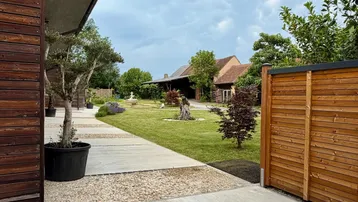 Blick auf den gepflegten Gartenbereich mit Bäumen und einem modernen Gebäude unter einem bewölkten Himmel.