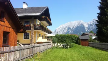 Traditionelles Haus mit gelber Fassade, Holzbalkonen und Bergblick in sonniger Umgebung.