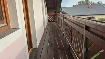 Langer, schmaler Holzbalkon mit Holzgeländer und Blick auf die Umgebung.