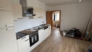Helle Küche mit Laminatboden und bereits installierten Unterschränken, Backofen und Dunstabzugshaube.