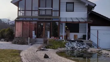 Modernes Einfamilienhaus mit großer Glasfassade, Teich und gepflastertem Weg im Vorgarten.