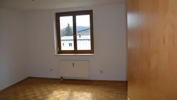 Leerer Raum mit Parkettboden, weiß gestrichenen Wänden und einem Fenster mit Bergblick.