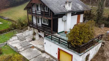 Freistehendes Haus mit mehreren Balkonen, Garage und umgebender Natur in nebliger Landschaft.