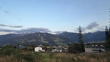 Weitläufiger Blick über die alpine Landschaft mit Häusern und bewaldeten Bergen bei Dämmerung.
