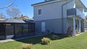 Modernes Haus mit gepflegtem Rasen, einem Wintergarten und einem kleinen Balkon im Obergeschoss.