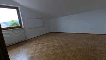 Helles Zimmer mit Parkettboden, weiß gestrichenen Wänden und einem Fenster mit Ausblick.