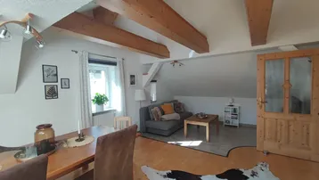 Gemütlicher Wohn- und Essbereich im Dachgeschoss mit Holzbalken und hellem Parkettboden.