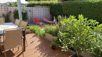 Sonniger Gartenbereich mit Holzterrasse, Liegestühlen und üppiger Bepflanzung.