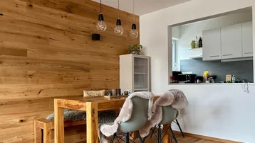 Gemütlicher Essbereich mit Holztisch, Sitzbank und Durchreiche zur Küche, umgeben von einer Holzwand.