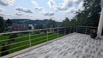 Große geflieste Terrasse mit Edelstahlgeländer und weitem Blick über die grüne Landschaft.