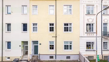 Fassade eines Mehrfamilienhauses mit mehreren Fenstern und Eingangsbereich in einer städtischen Umgebung.