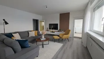 Helles Wohnzimmer mit modernem Sofa, Holzwandakzent und Zugang zum Balkon.