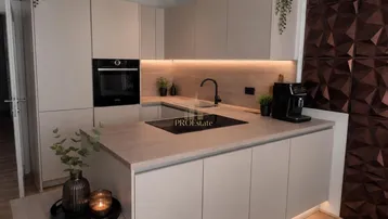 Moderne Küche mit hellgrauen Schränken, Holzarbeitsplatten, integriertem Backofen und Induktionskochfeld.