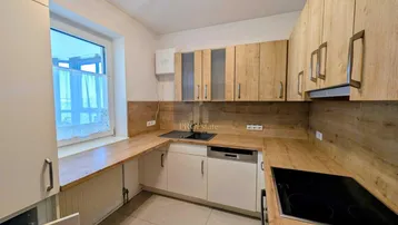Funktionale Küche mit hellen Holzfronten, weißen Unterschränken und integrierten Geräten sowie einem Fenster.
