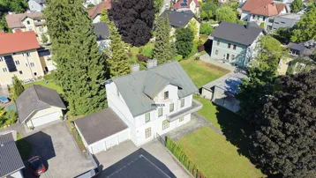 Luftaufnahme eines Hauses mit Satteldach und umliegender Wohnbebauung in grüner Umgebung.