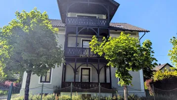 Historisches Gebäude mit charakteristischen Holzveranden und Balkonen, umgeben von grünen Bäumen.