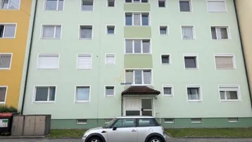 Ansicht der Gebäudefassade eines Mehrfamilienhauses mit hellgrüner Farbgebung und vielen Fenstern.