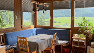 Heller Essbereich mit Holztäfelung, blauen Sitzbänken und weitem Blick ins Grüne durch große Fenster.