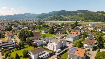 Weitläufige Luftaufnahme einer Wohngegend mit Bergen im Hintergrund und viel Grün.