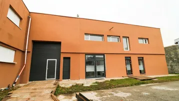 Moderne Gewerbeimmobilie mit orangefarbener Fassade, großen Toren und Fenstern, bereit zur Nutzung.