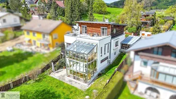 Luftaufnahme des modernen Hauses mit großer Glasfassade, Dachterrasse und grüner Umgebung.