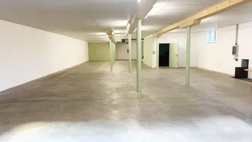 Großer, leerer Raum mit Betonboden, weißen Wänden und grünen Stützpfeilern, ideal für Lager oder Produktion.