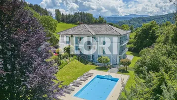 Großzügiges Anwesen mit privatem Pool, umgeben von üppigem Grün und malerischer Berglandschaft unter blauem Himmel.