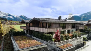 Modernes Wohnhaus mit Holzfassade, begrüntem Dach und Bergblick in alpiner Umgebung.
