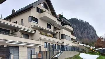 Modernes Mehrfamilienhaus mit mehreren Balkonen und Blick auf die umliegende Berglandschaft.