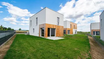 Moderne Neubauhäuser mit weißer Fassade und Holzverkleidung, umgeben von grünen Rasenflächen unter blauem Himmel.
