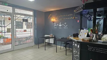 Innenansicht eines kleinen Restaurants oder Imbisses mit Theke und Sitzgelegenheiten. Große Fensterfront zur Straße.