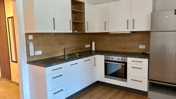 Moderne Einbauküche mit weißen Schränken, dunkler Arbeitsplatte und integrierten Geräten.