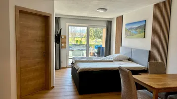 Helles Schlafzimmer mit Doppelbett, kleinem Essbereich und Zugang zu einem Außenbereich.