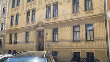 Historisches Gebäude mit reich verzierter Fassade und parkenden Autos davor in der Stadt.
